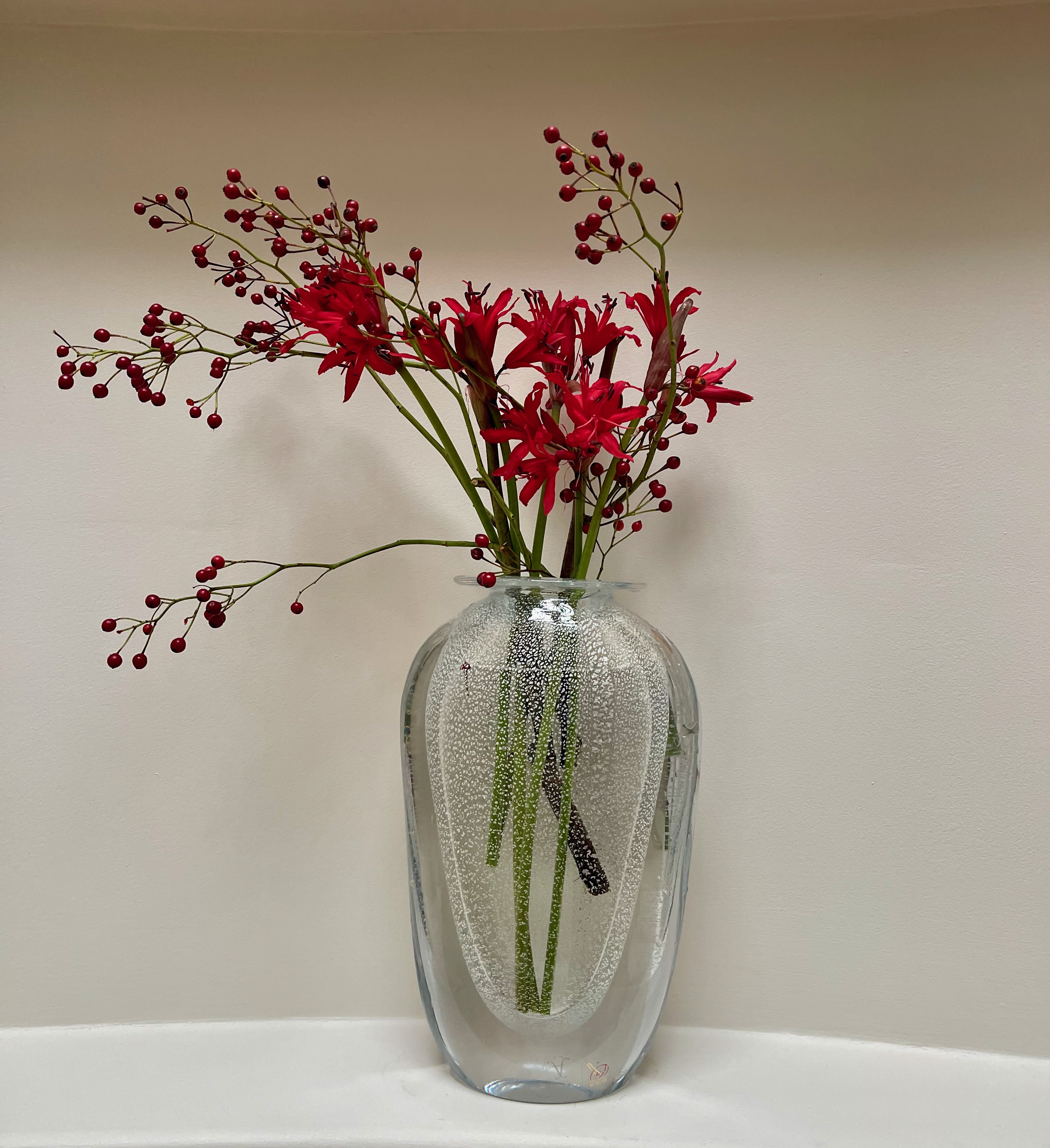 Red flowers and fine branching stems arranged with space and movement in a clear glass vase