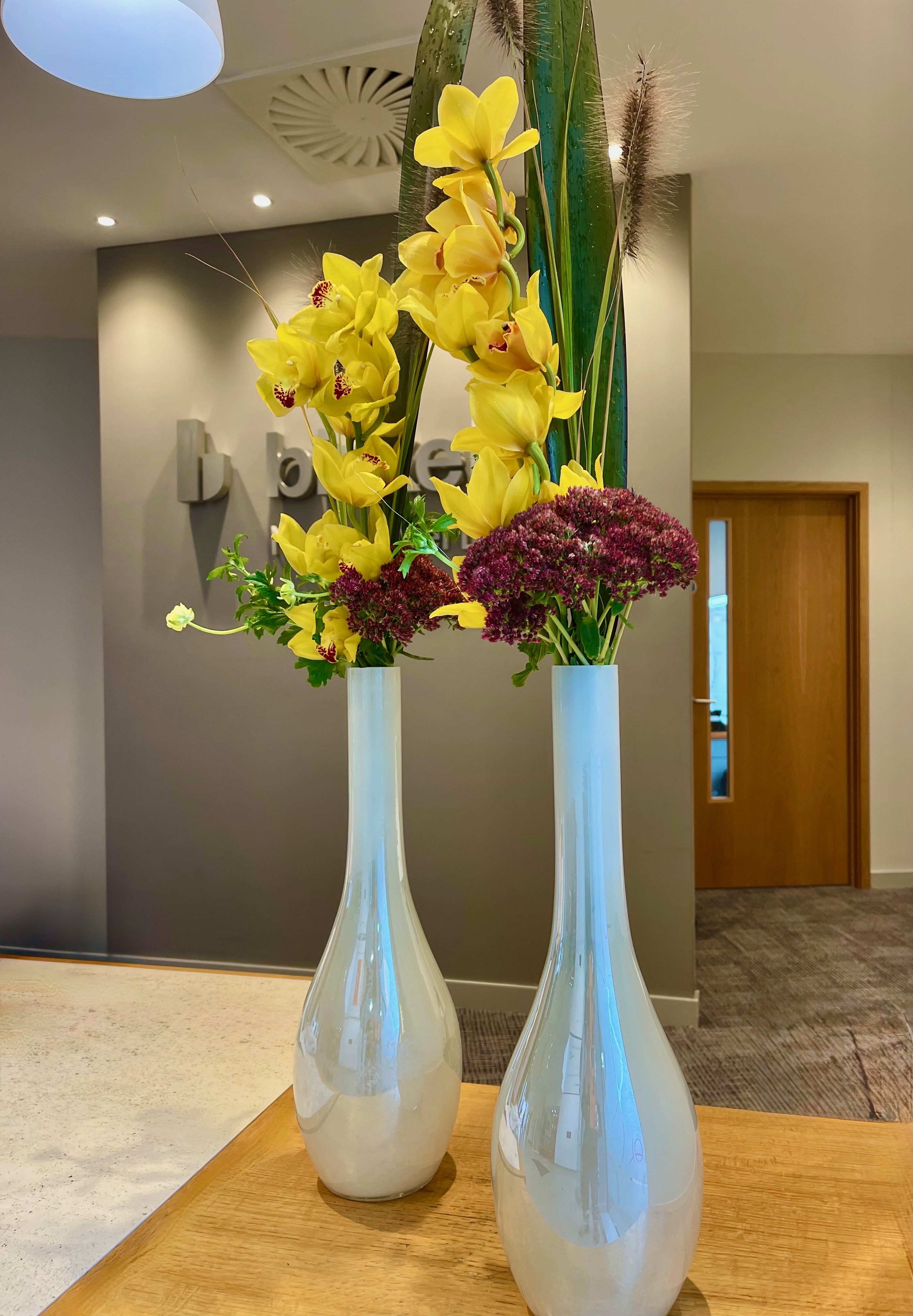 Yellow orchids and tall stems arranged in two slender pale vessels