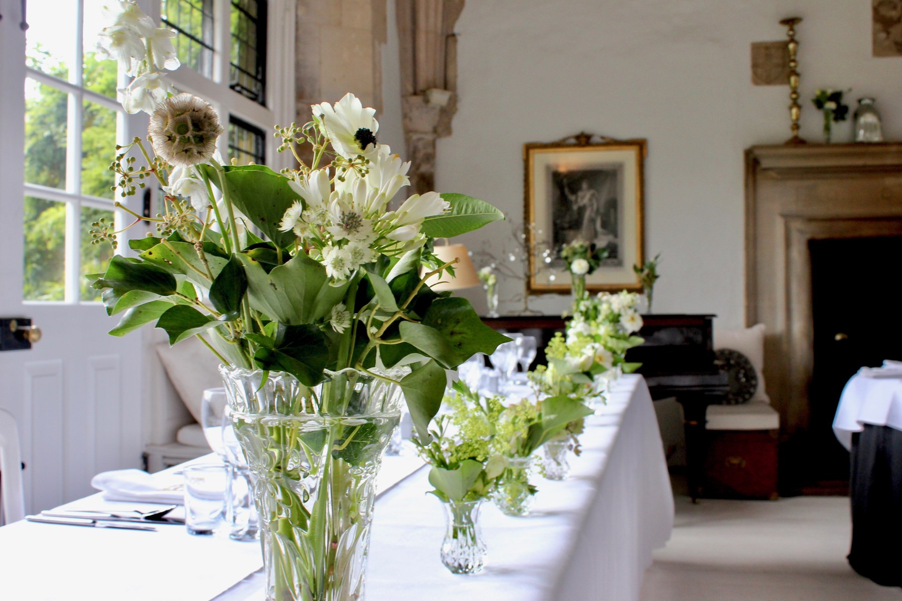 White and green flowers in clear glass vases in the light-filled dining room at Butley Priory