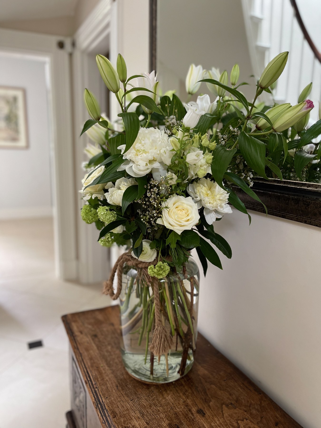 White lilies, roses and seasonal flowers in a glass vase on a wooden table in a home