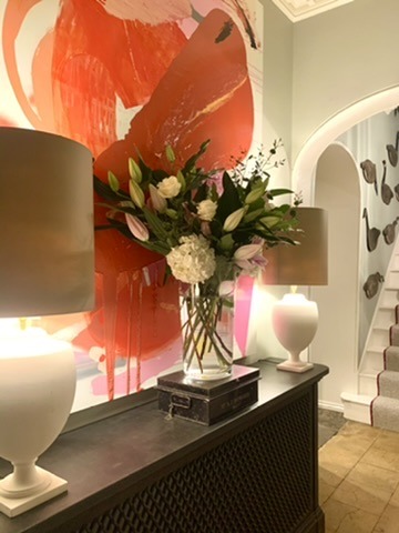 A generous vase of white flowers and foliage between two lamps, against a vivid orange artwork