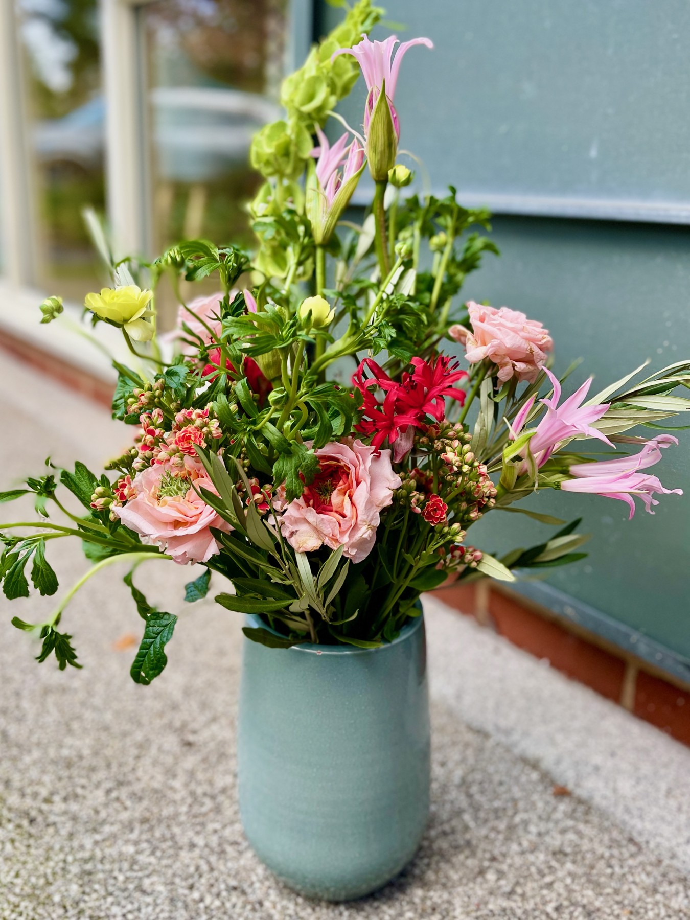 Pink roses and nerines with red flowers and fresh green stems in a grey ceramic vase
