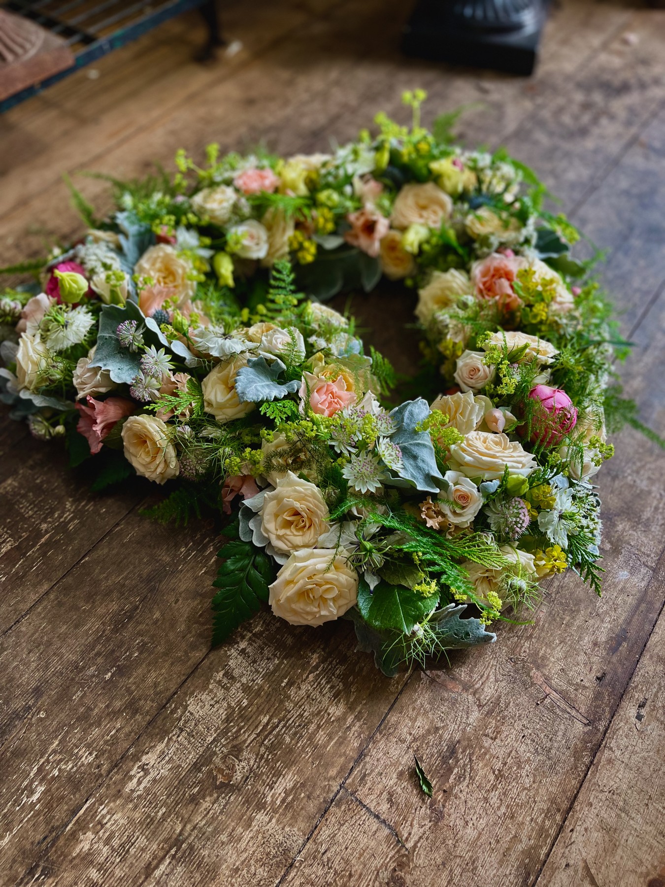 An open floral heart of cream and soft peach roses with green foliage and delicate blue flowers