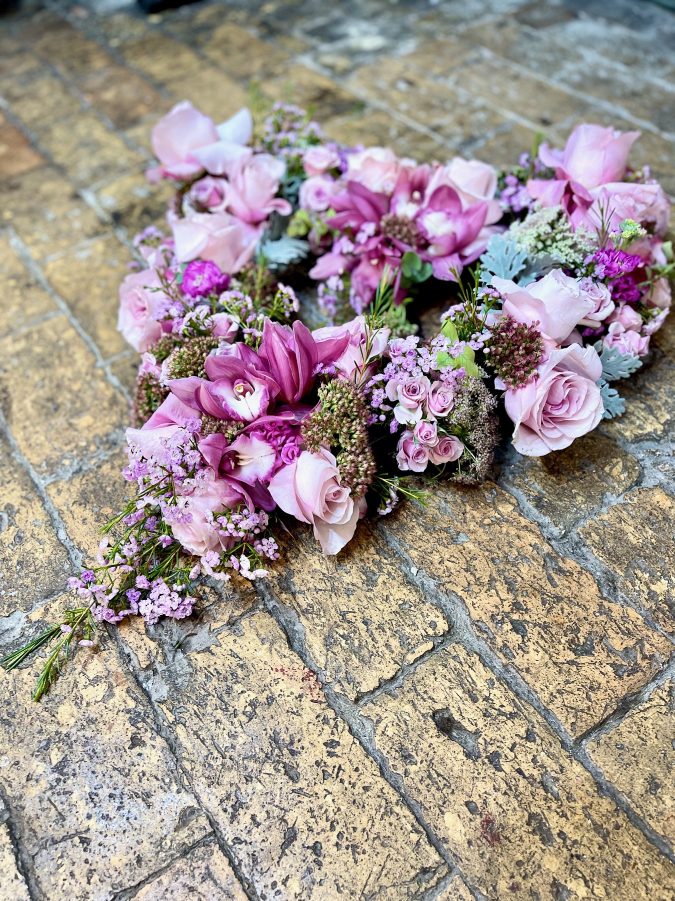 A floral heart with pink orchids, lilac flowers and delicate foliage on a stone surface