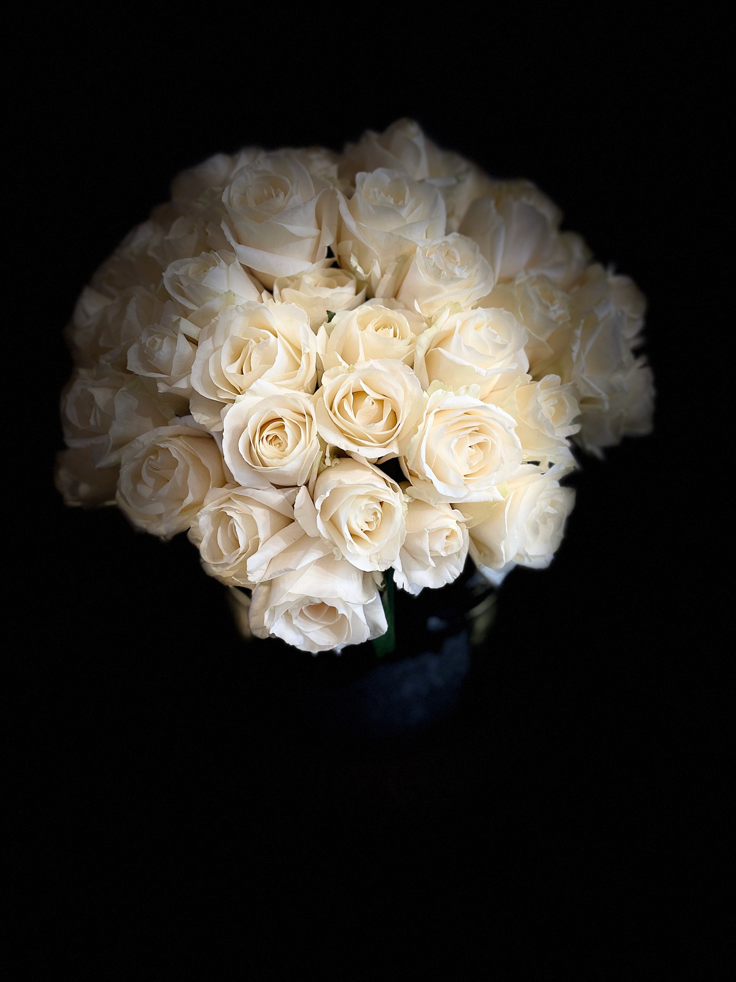 A generous bouquet of white and cream roses photographed against a dark background