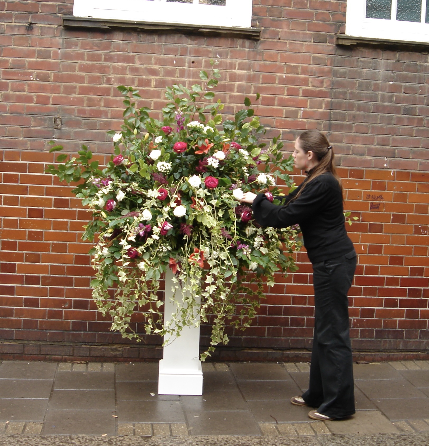 Sally making her first large pedestal arrangement while training with Michael, with pink and white flowers and trailing foliage