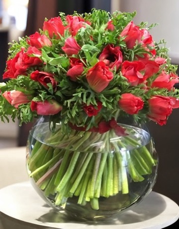 A rounded red and pink bouquet in a glass vase with the spiralled stems clearly visible