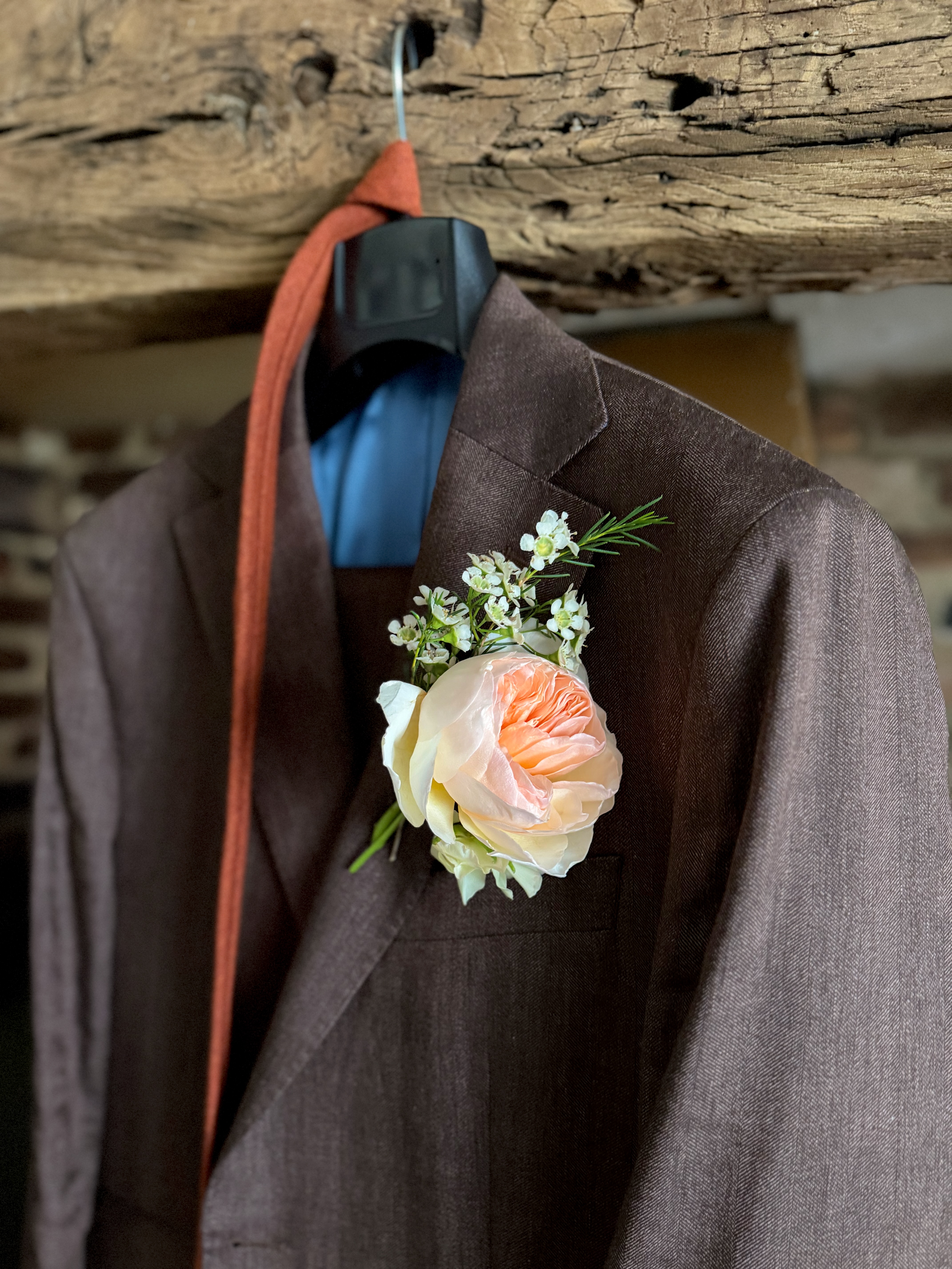 A peach rose and delicate white flowers worn as a buttonhole on a brown jacket