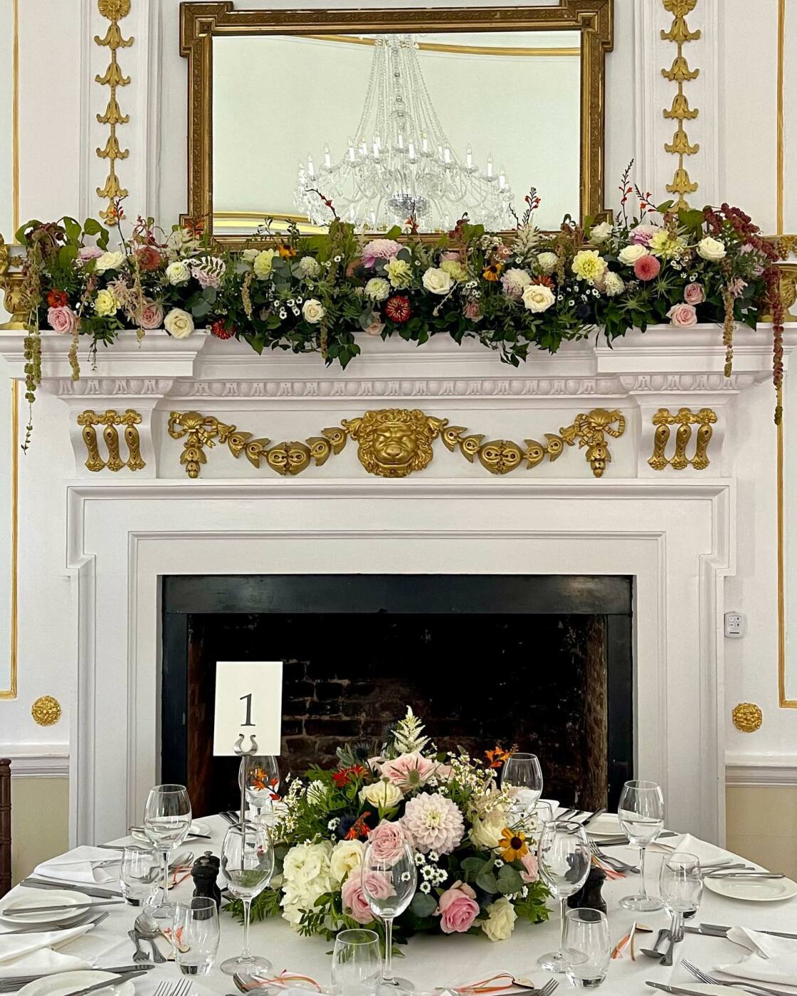 Seasonal wedding flowers across an ornate mantelpiece and reception table at Hintlesham Hall