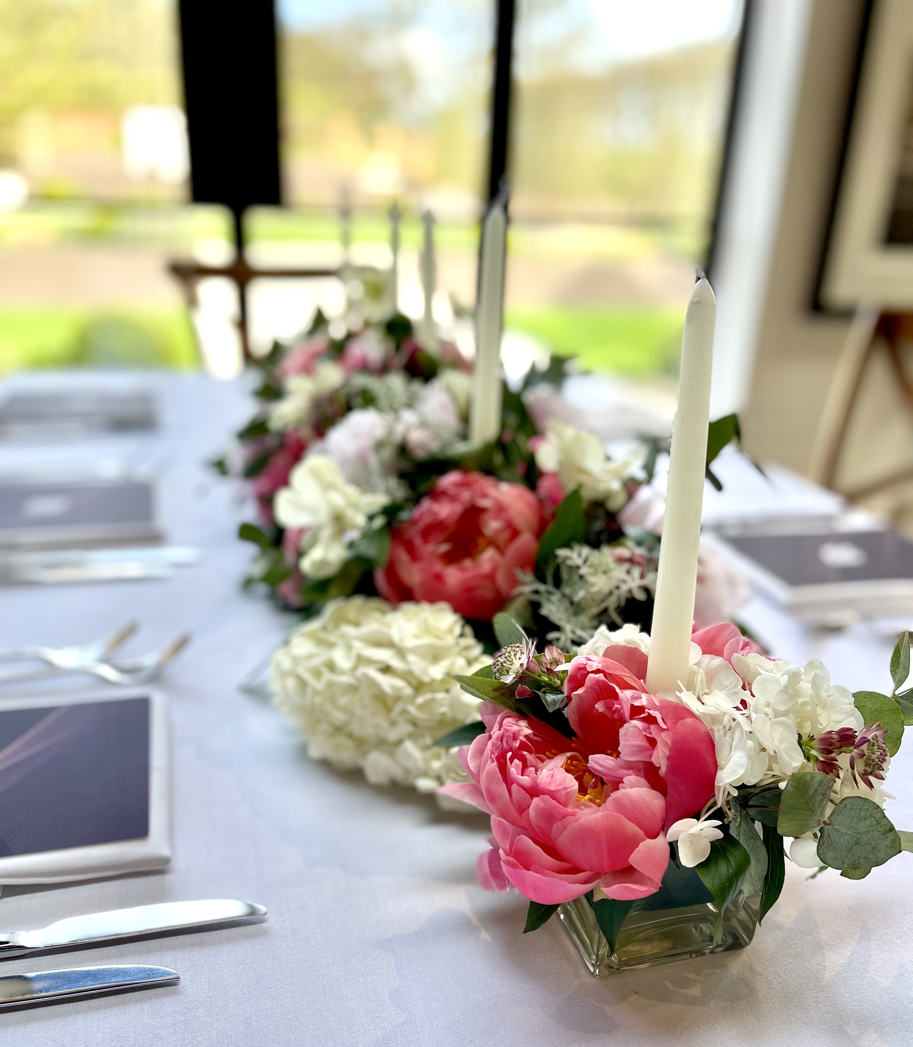 Pink peonies and white flowers with slender candles along a wedding reception table