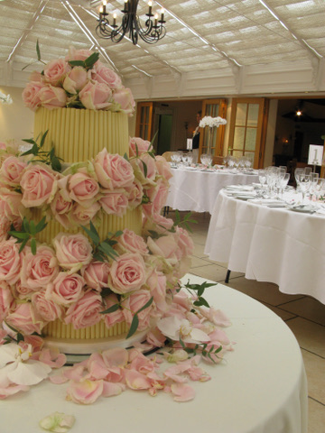 A tiered wedding cake decorated with pale pink roses and scattered rose petals