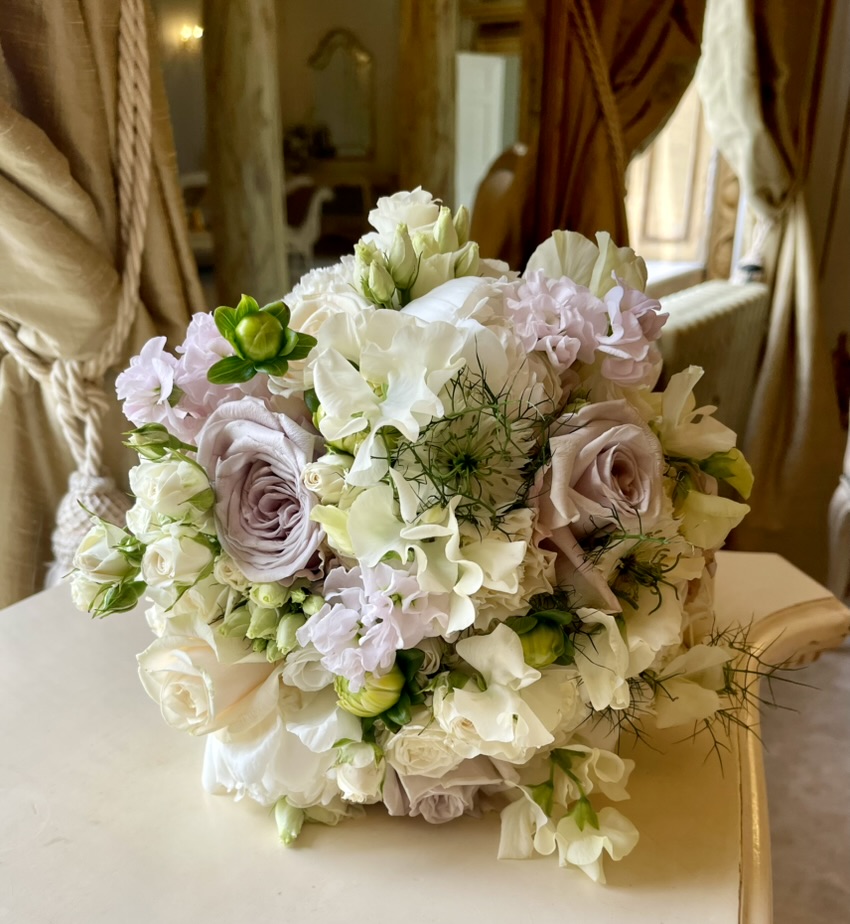 A rounded bridal bouquet of ivory and pale lavender flowers with roses and delicate green detail