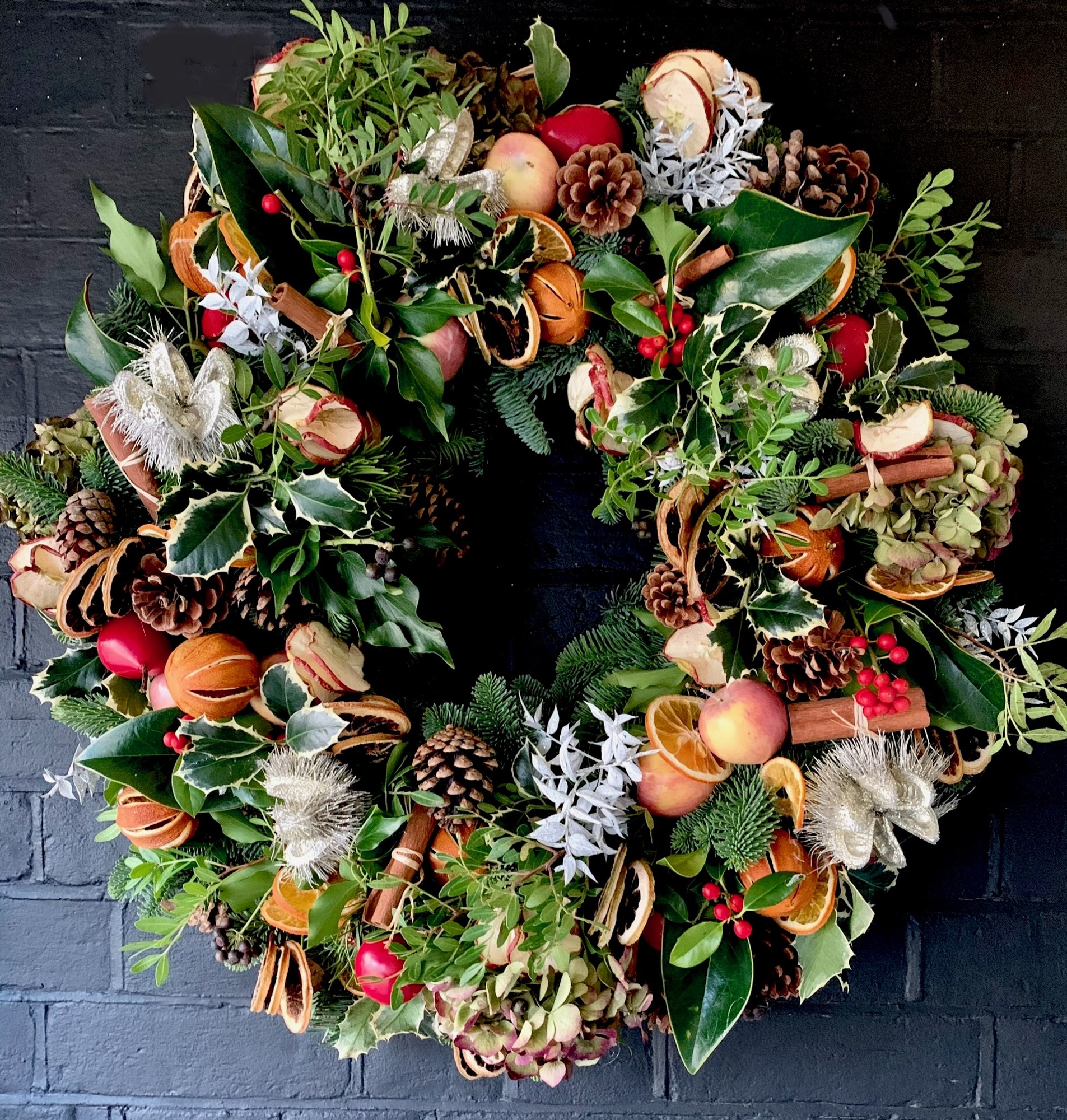 A richly textured wreath with evergreen foliage, orange slices, cones and fruit