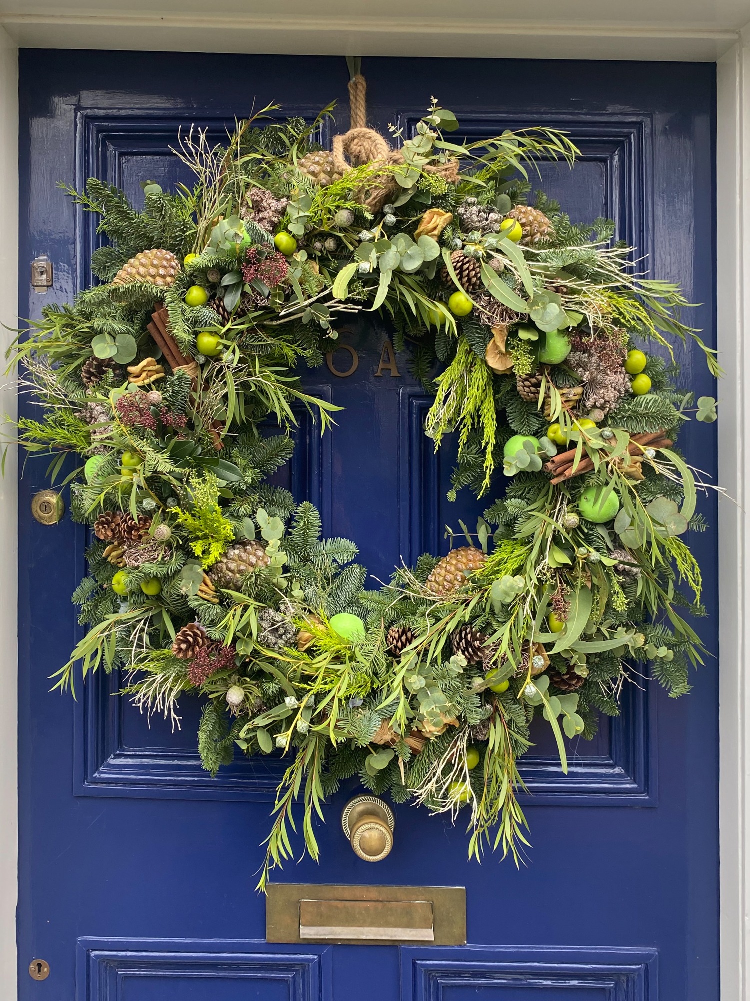 A loose natural wreath of mixed green foliage, fruit and seasonal details on a blue door