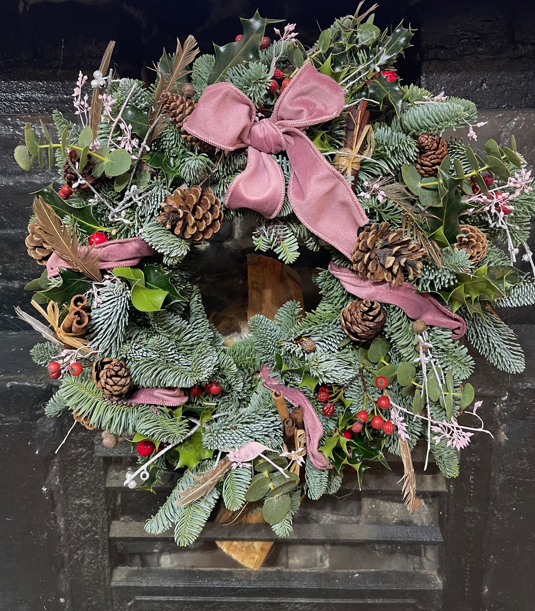An evergreen wreath with pine cones, flowers and a generous soft pink ribbon