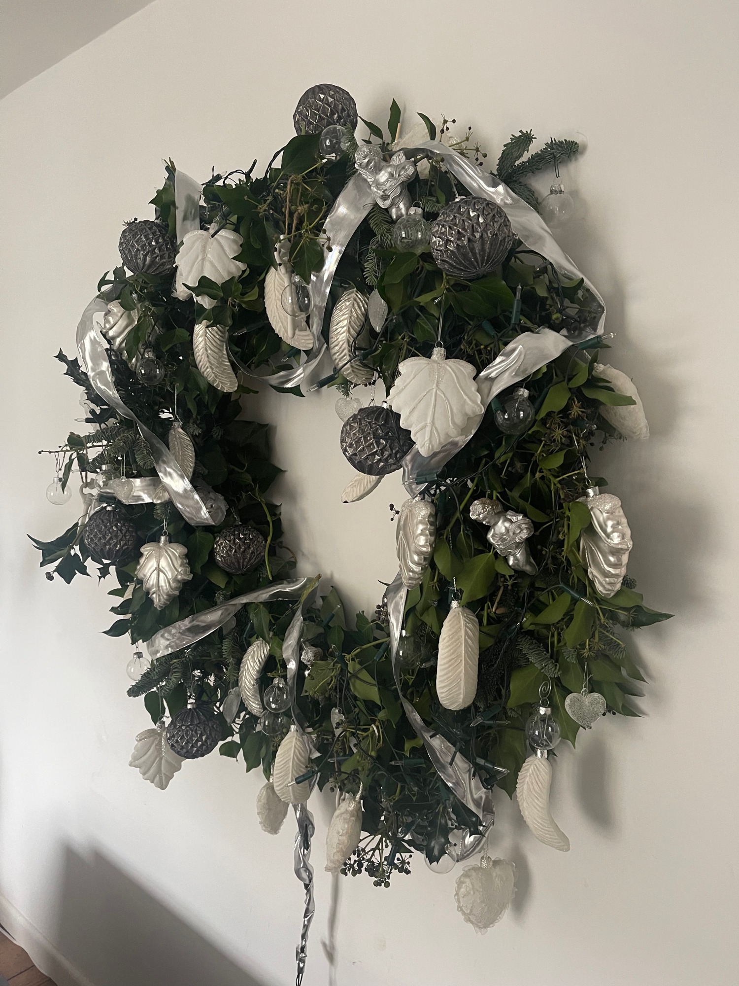 A white and green seasonal wreath with flowers and pale ribbon against a light wall